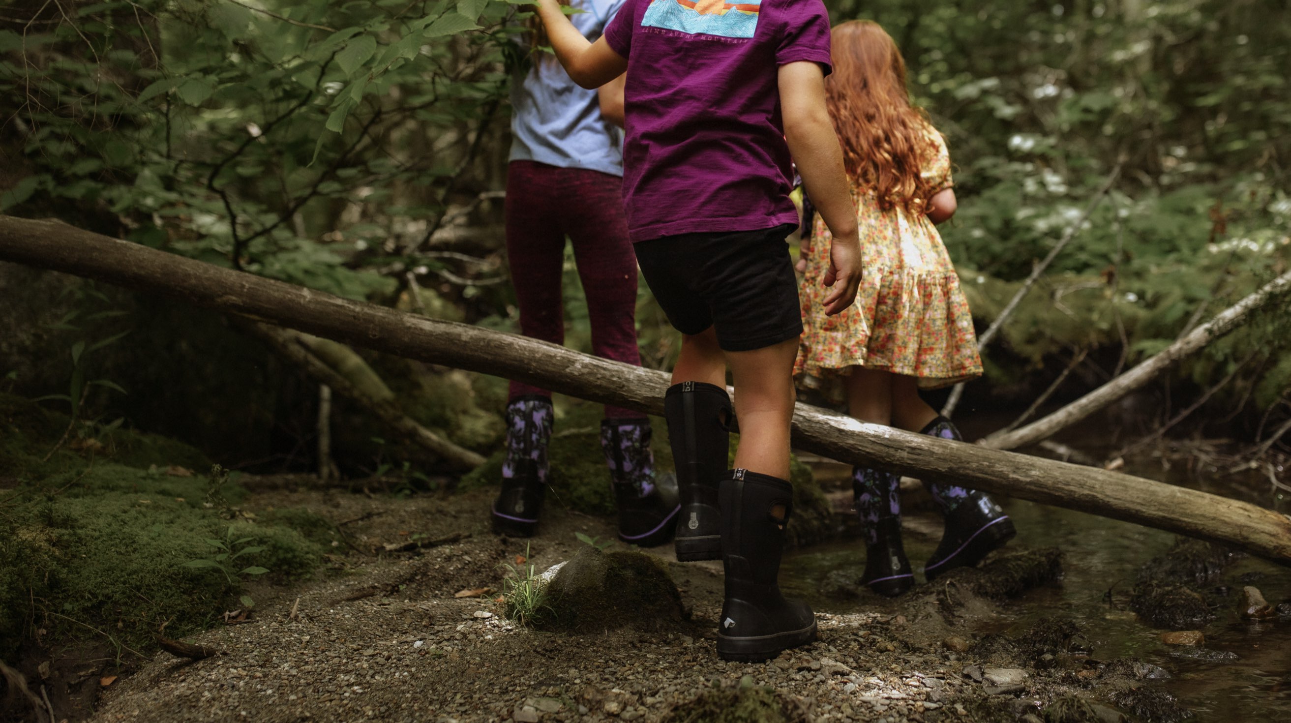 Click to shop Kids' Classic II boots. Image features the Kids' Classic boot in black walking through a dense wooden trail area