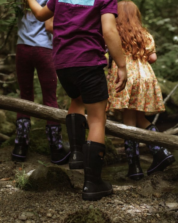 Click to shop Kids' Classic II boots. Image features the Kids' Classic boot in black walking through a dense wooden trail area