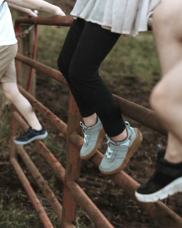 Click to shop the Kids Skyline Kicker featuring kids sitting on an old gate.