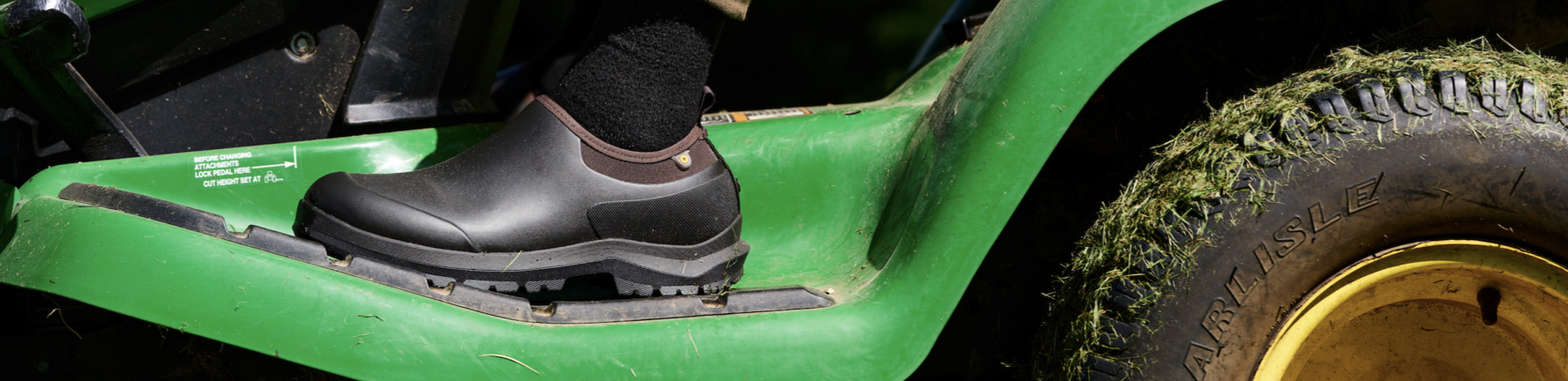 Shop our Men's Sauvie II Slip On in black.  The image shown is a closeup of the boot on a green tractor.