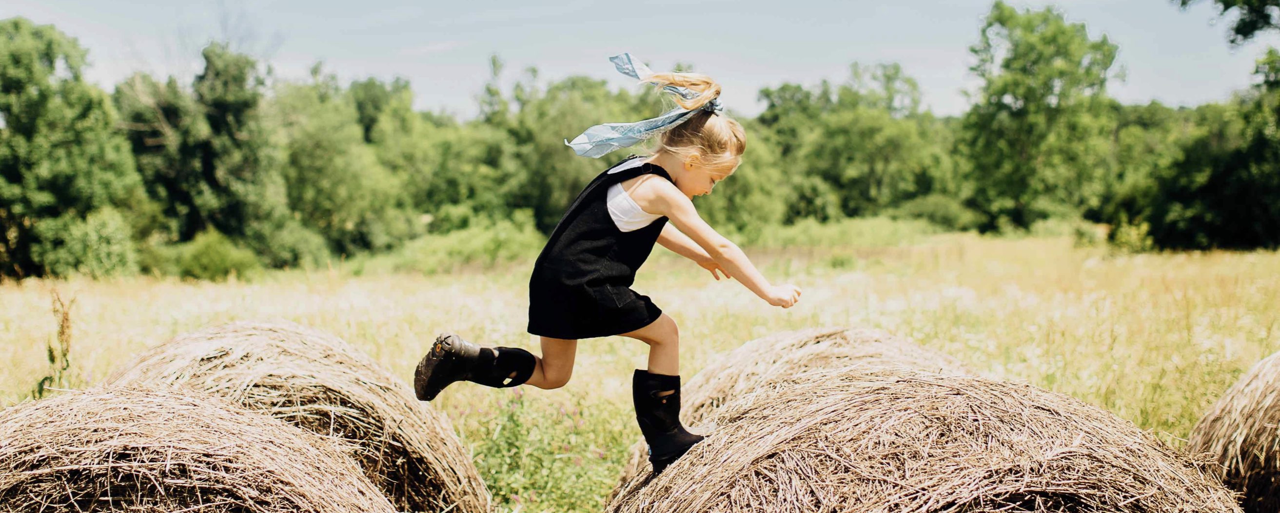 Shop kids' boots featuring a girl jumping on hay bales.