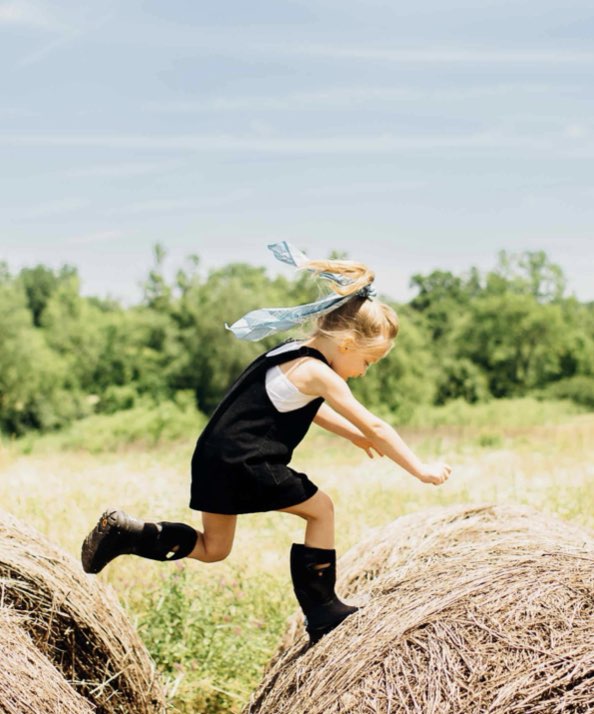Shop kids' boots featuring a girl jumping on hay bales.