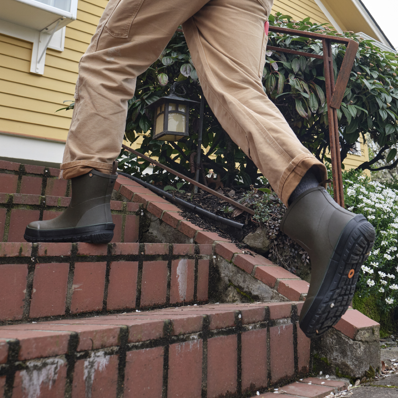 A man running up the stairs outside of his house wearing the Men's Digger mid yard & garden boots in a green colorway.
