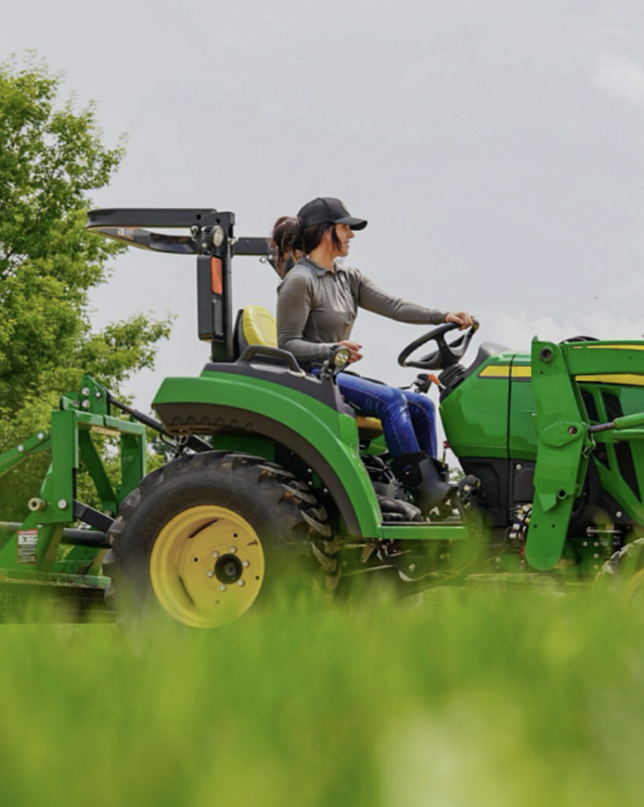 A woman riding a tractor.  Shop our Women's Farm & Work boots.