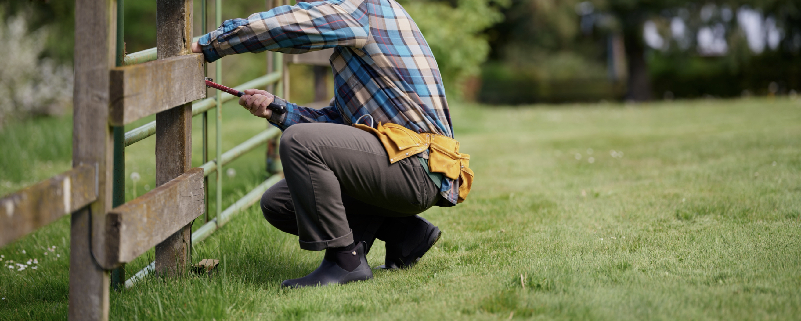 A person using a hammer to fix a fence.  Shop our Fall Chores boots.