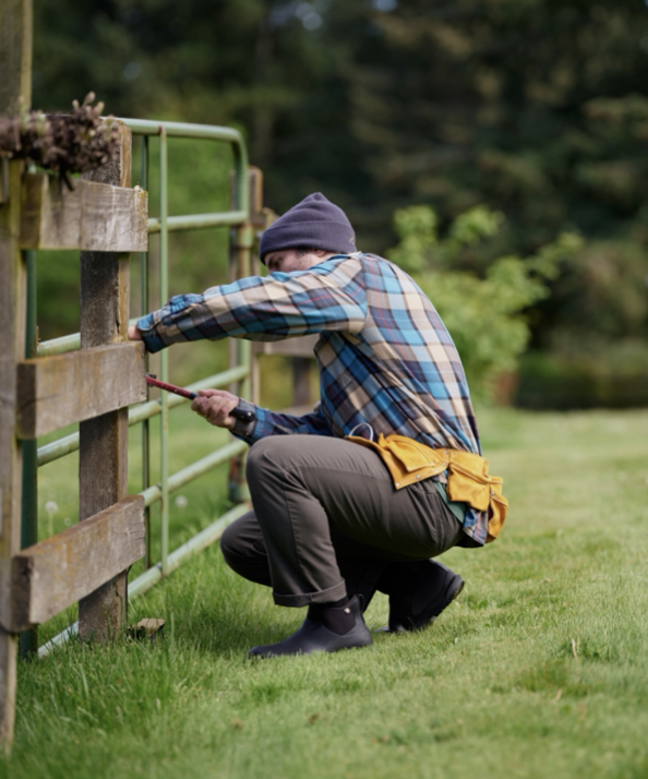 A person using a hammer to fix a fence.  Shop our Fall Chores boots.