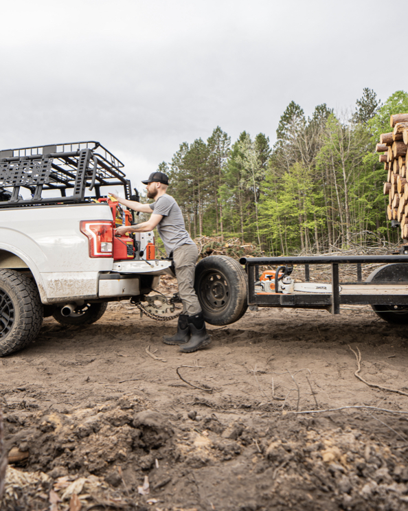 A guy pulling out of heavy equipment out of a truck with a trailer of logs. Shop our Men's Classic Seamless boots in black
