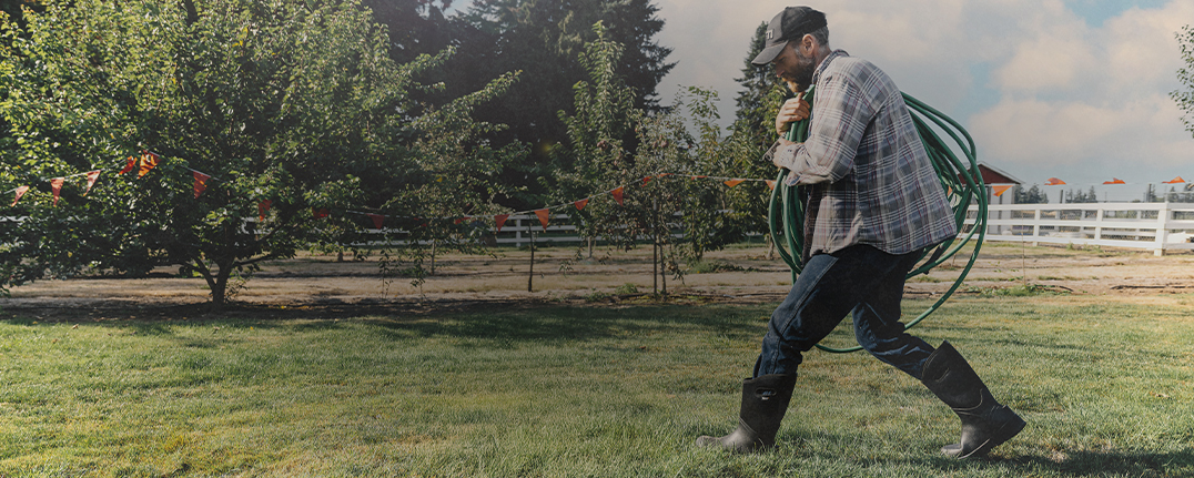 Shop our favorite spring styles featuring a man carrying a garden hose across a yard. 