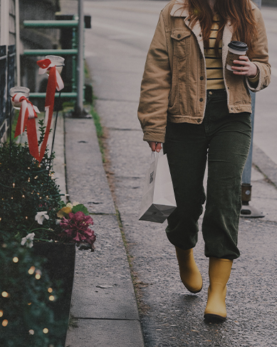 Shop our holiday gift guide featuring a woman walking by a store with holiday decorations.