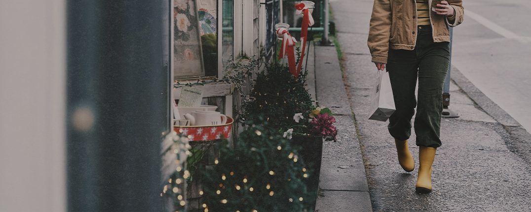 Shop our holiday gift guide featuring a woman walking by a store with holiday decorations.
