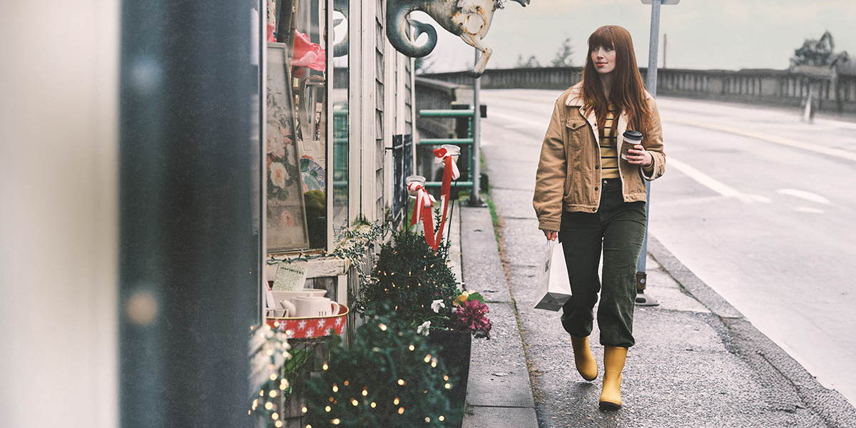 Shop our holiday gift guide featuring a woman walking by a store with holiday decorations.