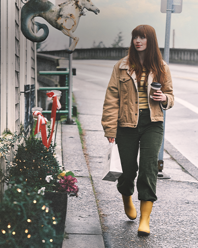 Shop our holiday gift guide featuring a woman walking by a store with holiday decorations.