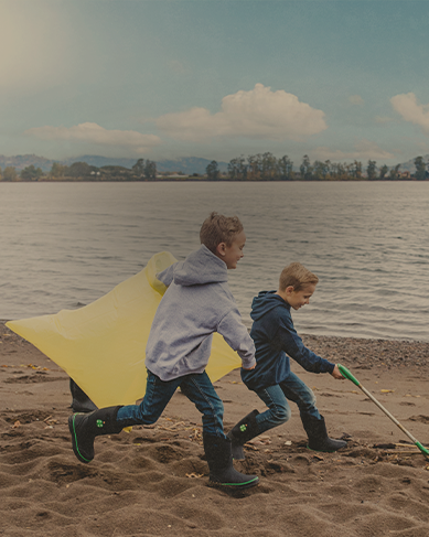 Shop Bogs kids' featuring 2 boys playing on a beach. 