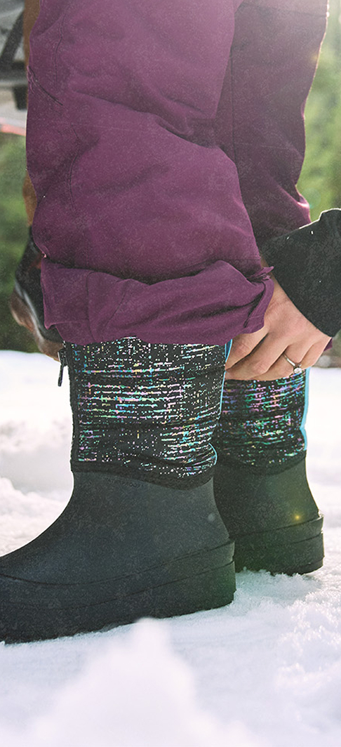 Kids' Easy On graphic. Images features a kid standing in snow while wearing BOGS Snow Shell Zip Metallic Stripes Kids' Winter Boots in Black Multi.