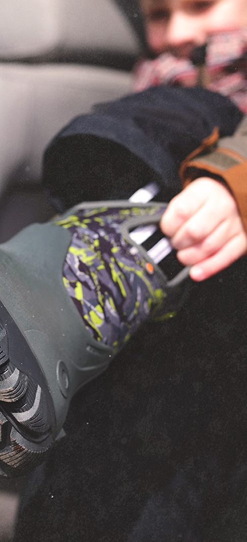 Kids' Easy On graphic. Image features a kid putting on BOGS Classic Seamless Edgy Camo Kids' Winter Boots in Dark Gray Multi using the BOGS signature handles.