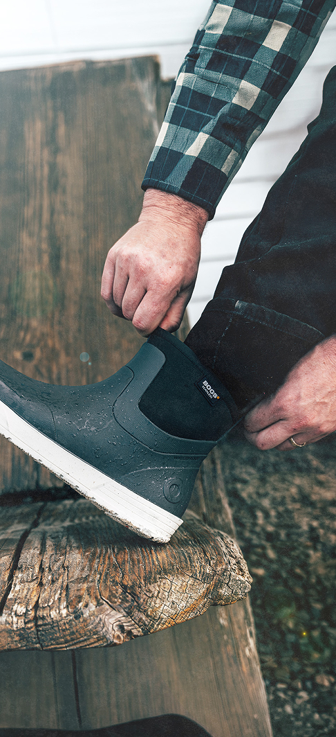 Unisex Easy On graphic. Image features a model putting on BOGS Rockaway Seamless Chelsea Slip-On Boots in Black Multi.