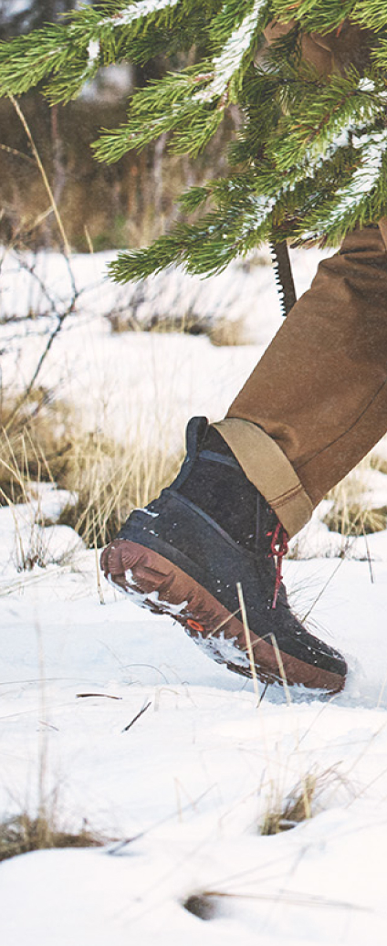Unisex Neo-Tech graphic. Image features a model walking in the snow wearing BOGS Neo-Tech boots.