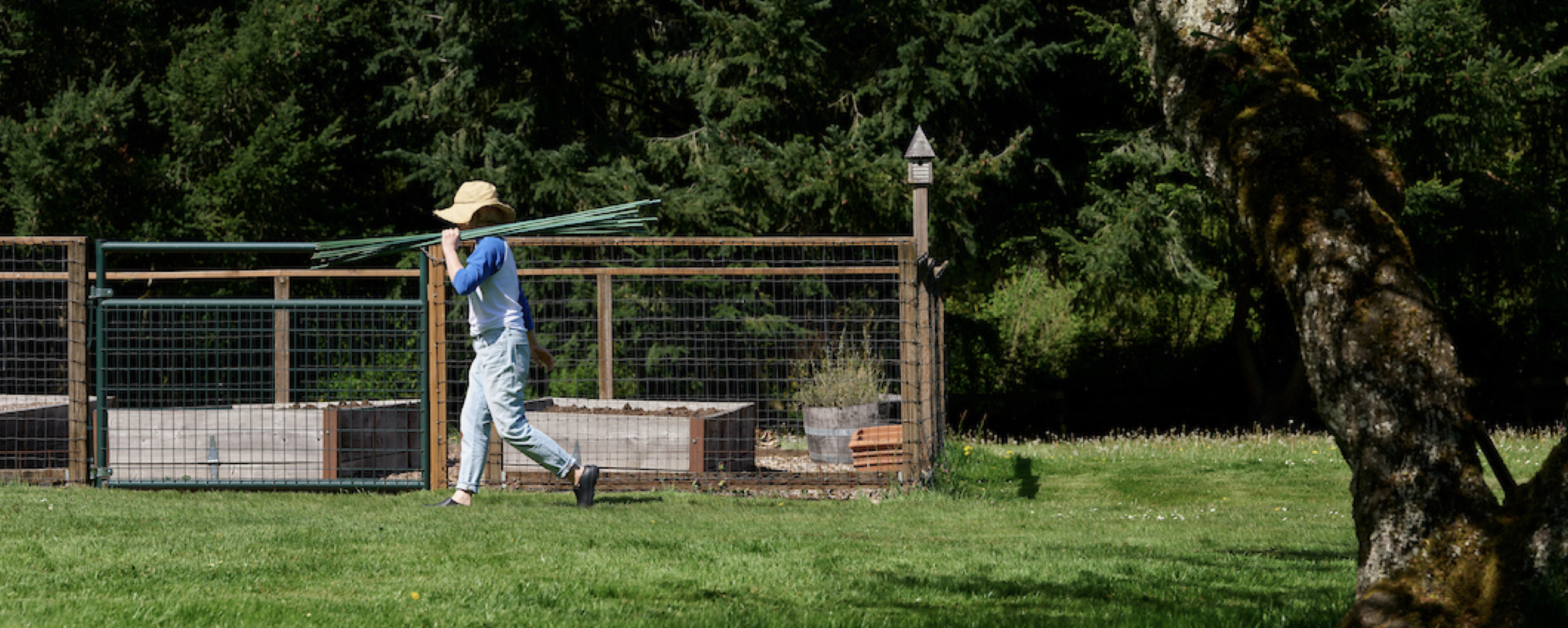 A woman walking with garden poles with garden beds in the background.  Shop our Yard and Garden Boots best sellers.