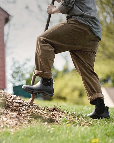 Image features a man in a black ankle boot shoveling mulch.