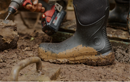 For the Hard Worker. Image shows a close up of a bogs boot covered in mud while using power tools.