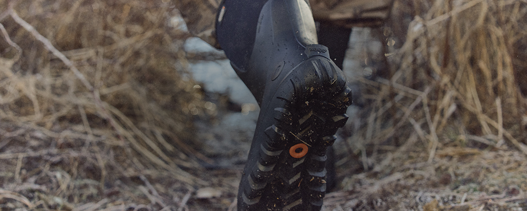 Image features a man wearing a black boot through dried brush.