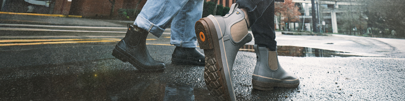 Image features a close-up of two models wearing BOGS                waterproof boots while walking down a street wet with rain.