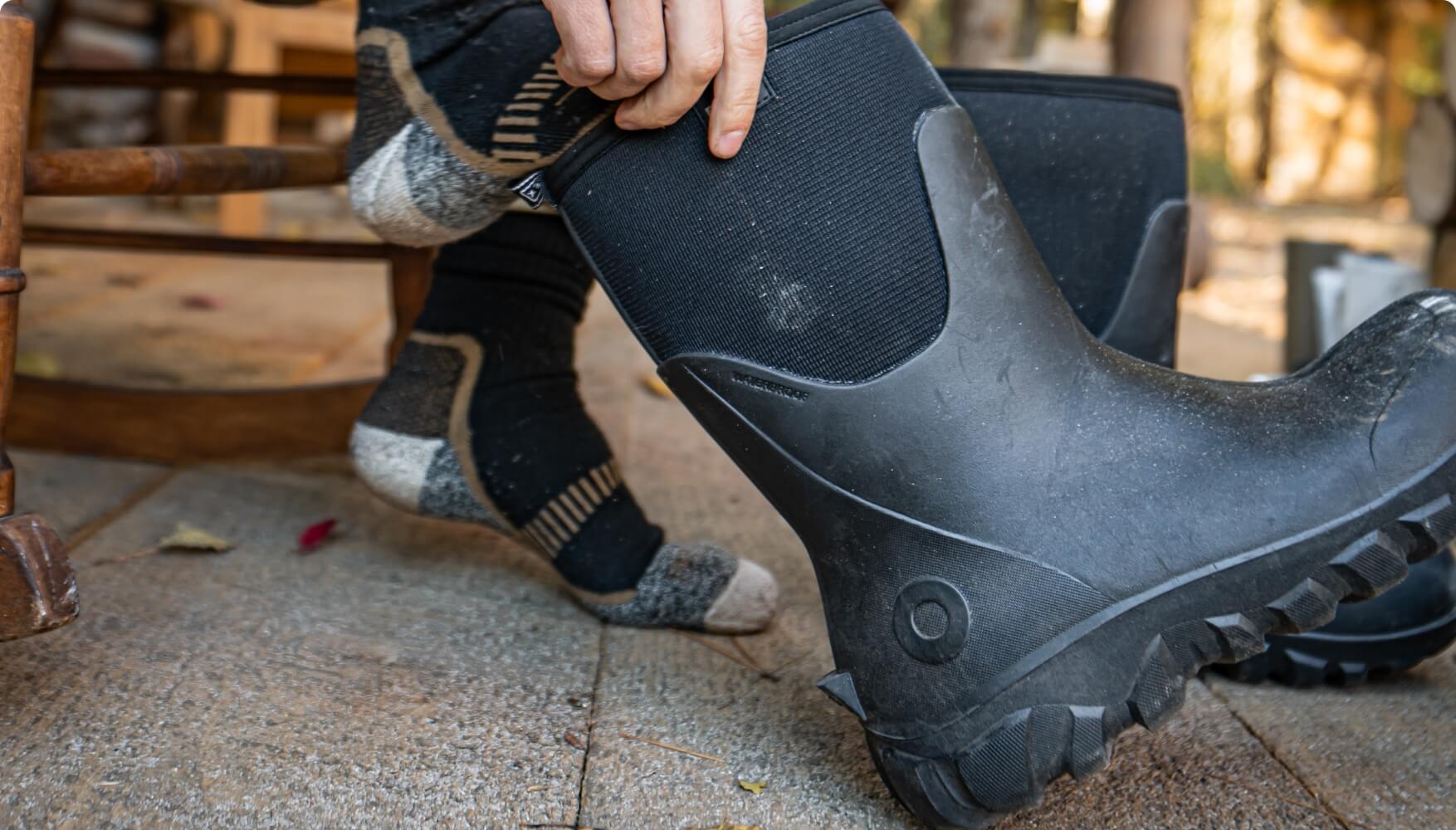 Image features a man putting on a pair of BOGS Classic Seamless                   Tall Boots in Black.