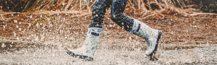 Image features a kid wearing rainboots running and splashing through a puddle.